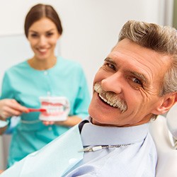 smiling older patient with a dental professional holding dentures and a toothbrush