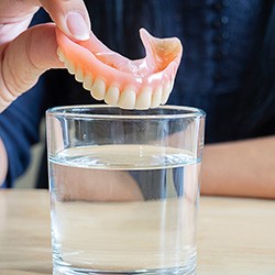 hand putting dentures in a glass of water