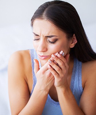 Woman on bed with toothache needing emergency dentist in Westhampton, NY