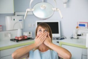 woman fearful of dental pain covering her mouth while in the dentist chair